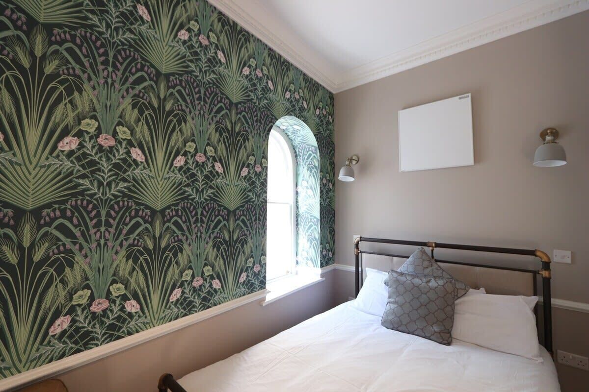 Une chambre à coucher avec un lit, une fenêtre, une lampe fixée au mur et un mur décoratif.