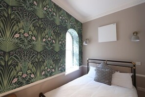 A bedroom with a bed, a window, a wall-mounted light, and a decorative wall. - Alma Studios - Apartment 4 - Hopewell (Bristol)