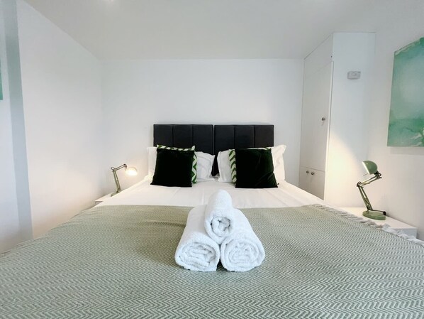 Habitación de hotel con una cama, dos lámparas de noche, un cabecero y una toalla sobre la cama.