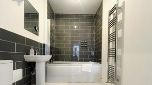 Ein Badezimmer mit Toilette, Waschbecken und Badewanne in Weiß sowie einer Duschkabine mit schwarzen Fliesen.