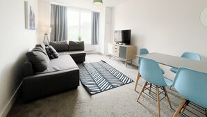 Ein modernes Wohnzimmer mit einer Couch, einem Fernseher, einem Esstisch und Stühlen.