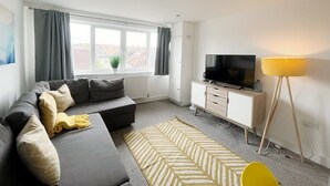 A modern living room with a sofa, television, cabinet, lamp, and a view of the city through large windows.