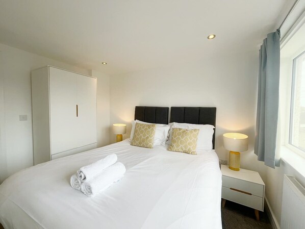 Habitación de hotel con cama, lámparas de noche, armario y ventana con cortinas.