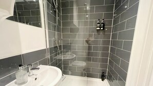 A bathroom with a white sink, a glass shower enclosure, and dark tiled walls.