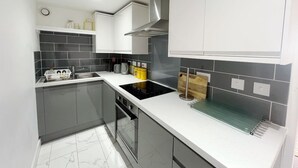 A modern kitchen with grey cabinets, a black countertop, a stove, and a sink.