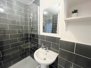 A bathroom with black tiles, a white sink, and a mirror. - Anstey Heights - Apartment 6 - Hopewell (Easton)