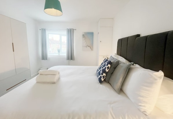 Una habitación de hotel moderna con una cama grande, cabecera, una ventana con cortinas, una obra de arte en la pared y un armario.