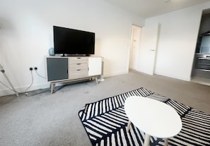 Una habitación con una televisión de pantalla plana sobre un mueble bajo, una mesa redonda pequeña y una alfombra a rayas.