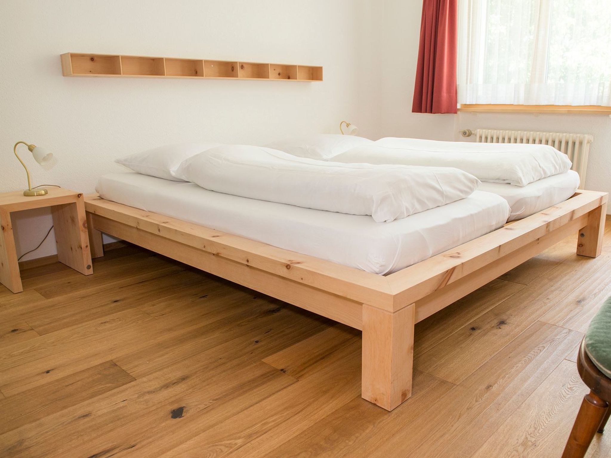 A wooden bed with white bedding in a room with wooden flooring and a white wall.