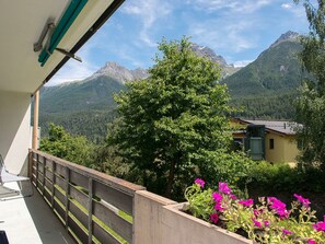 A balcony with a view of a mountain landscape, a wooden railing, and a flower bed with pink flowers. - LANIUS, (Scuol) by Interhome (Scuol)