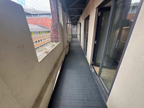 Ein schmaler Korridor mit einer schwarzen Gummimatte, Glastüren und Blick auf ein Gebäude mit roten Ziegeln und Fenstern.