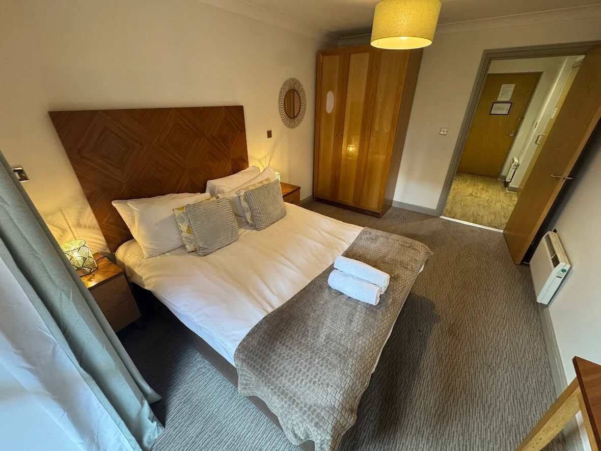 Une chambre d’hôtel avec un lit, une armoire en bois, une table de chevet avec une lampe et un miroir au mur.