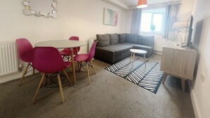 Uma sala de estar moderna com um sofá cinzento, uma mesa redonda com cadeiras cor-de-rosa, um tapete preto e branco e luminárias pendentes.