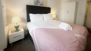 Quarto de hotel com uma cama, uma mesa de cabeceira com abajur, uma luminária pendente vermelha e um quadro na parede.