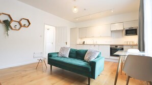 Un salon moderne avec un canapé vert, une petite table d’appoint et un coin repas comprenant une table et des chaises blanches.