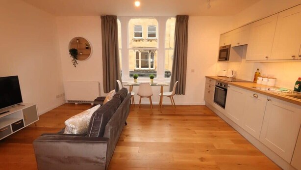 Een woonkamer met een bank, een televisie en een eethoek met een tafel en stoelen.
