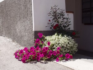 A building with a concrete facade and a flower bed with pink and white flowers. - Vidos 270, (Sent) by Interhome (Sent)