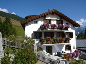 A two-story building with balconies adorned with flowers, a stone fence, and a mountainous backdrop. - Vidos 270, (Sent) by Interhome (Sent)
