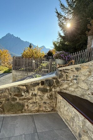 A stone bench with a view of mountains, a wooden fence, and a potted plant. - Vidos 270, (Sent) by Interhome (Sent)
