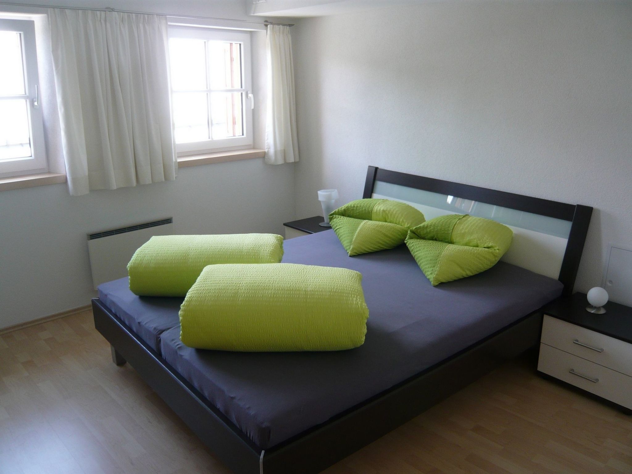 A bedroom with a bed, pillows, a bedside table, a lamp, and a window.