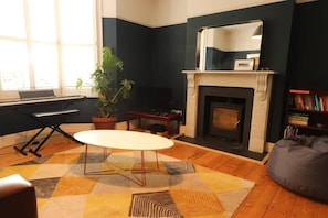 Uma sala de estar com um piano, lareira, mesa e estante de livros.