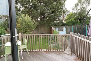Een houten terras met een hekwerk, een kleine tuin en een blauwe schuur op de achtergrond.