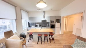 Een moderne keuken met een centraal eiland, barkrukken en een eettafel.