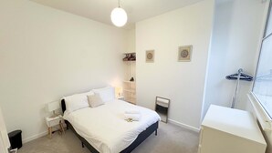 Een slaapkamer met een bed, nachtkastjes, een hanglamp, een raam met uitzicht en een kapstok.