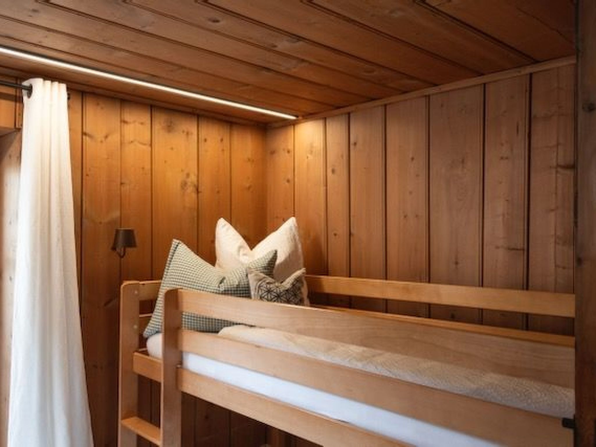Ein Holzbett mit Etagen, Kissen, eine Holzwand und ein Vorhang.