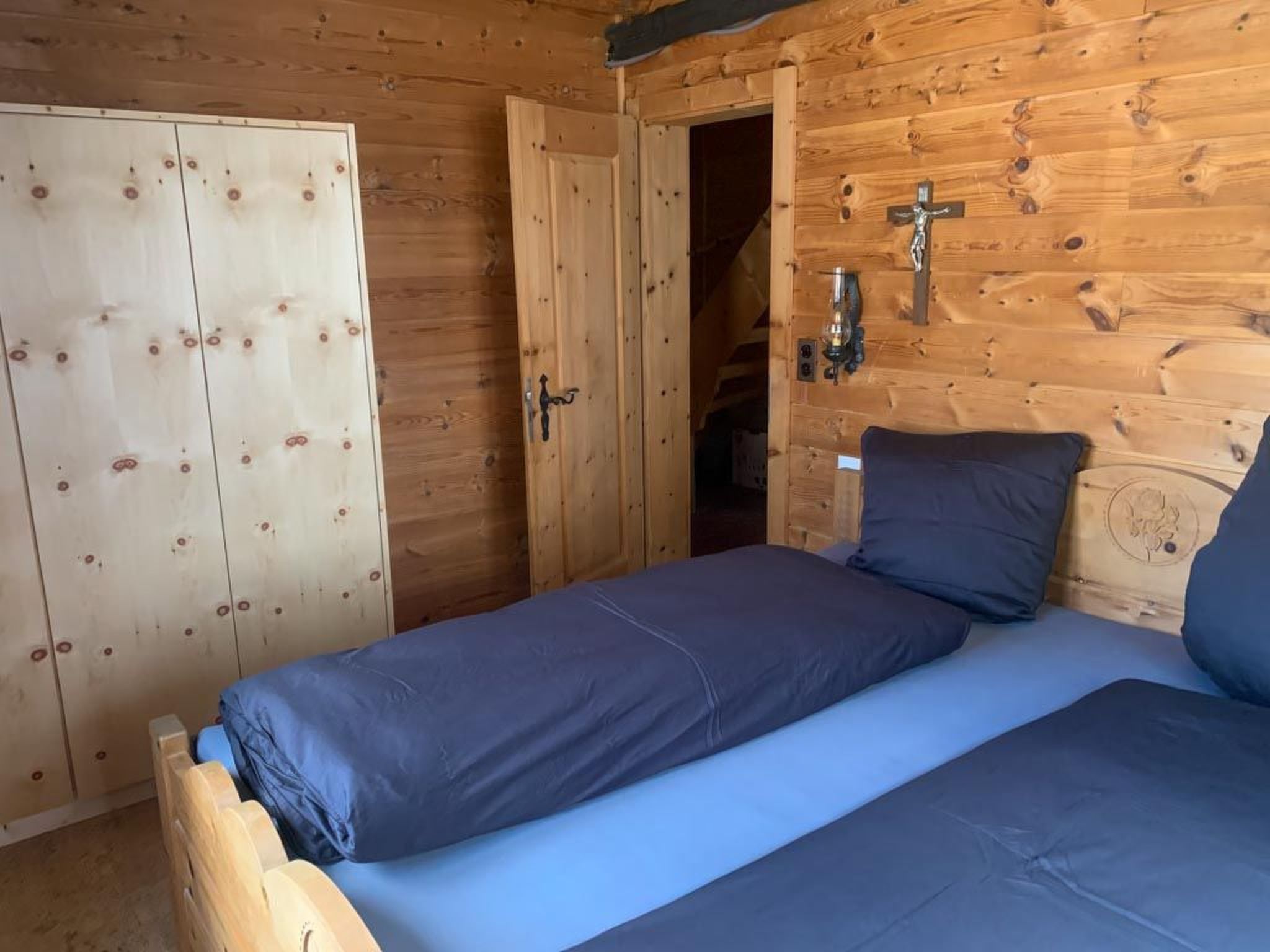 A wooden room with a bed, a wardrobe, and a door leading to another room.