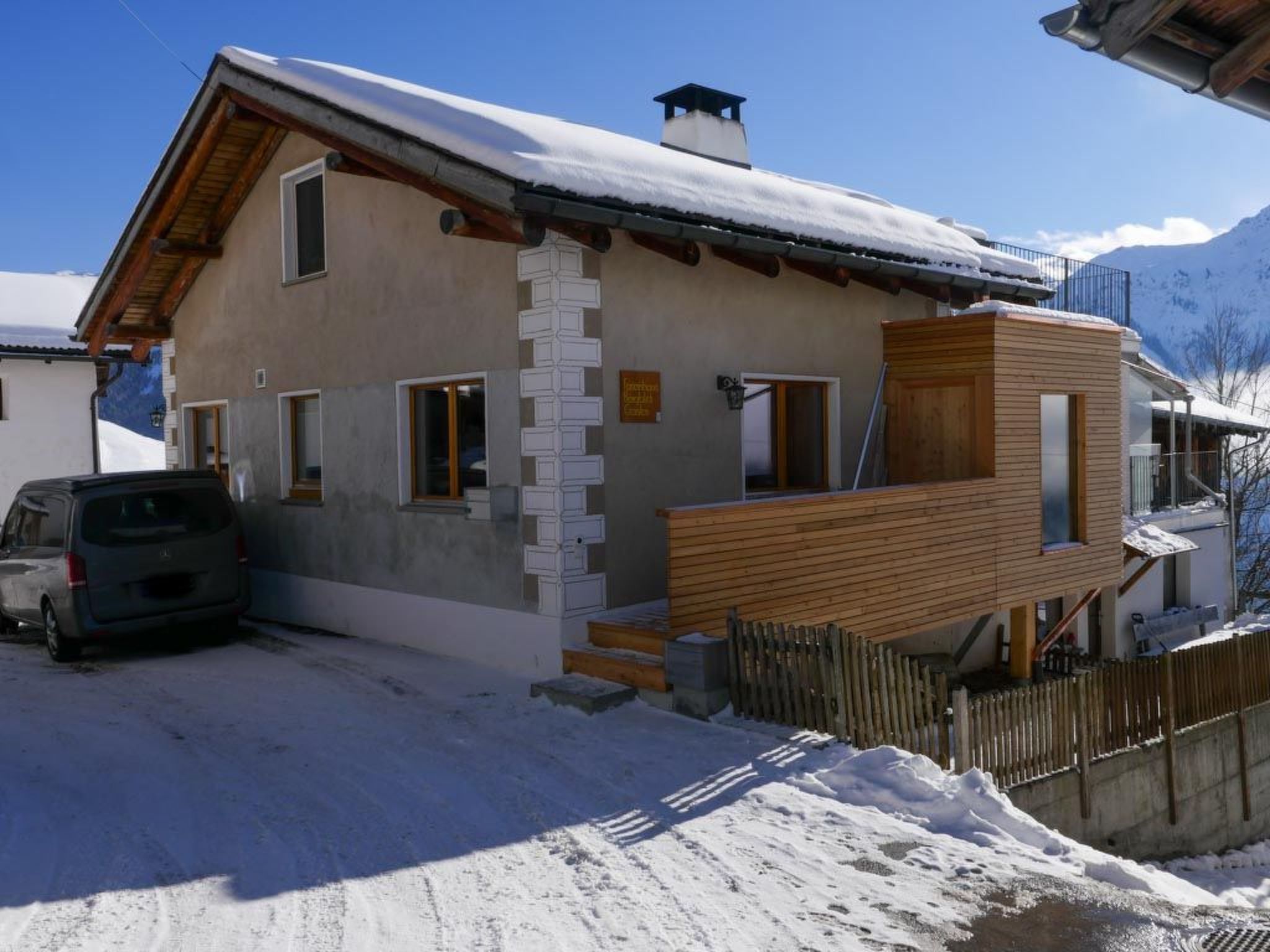Un edificio de dos pisos con techo nevado, una escalera de madera y un coche estacionado al frente.