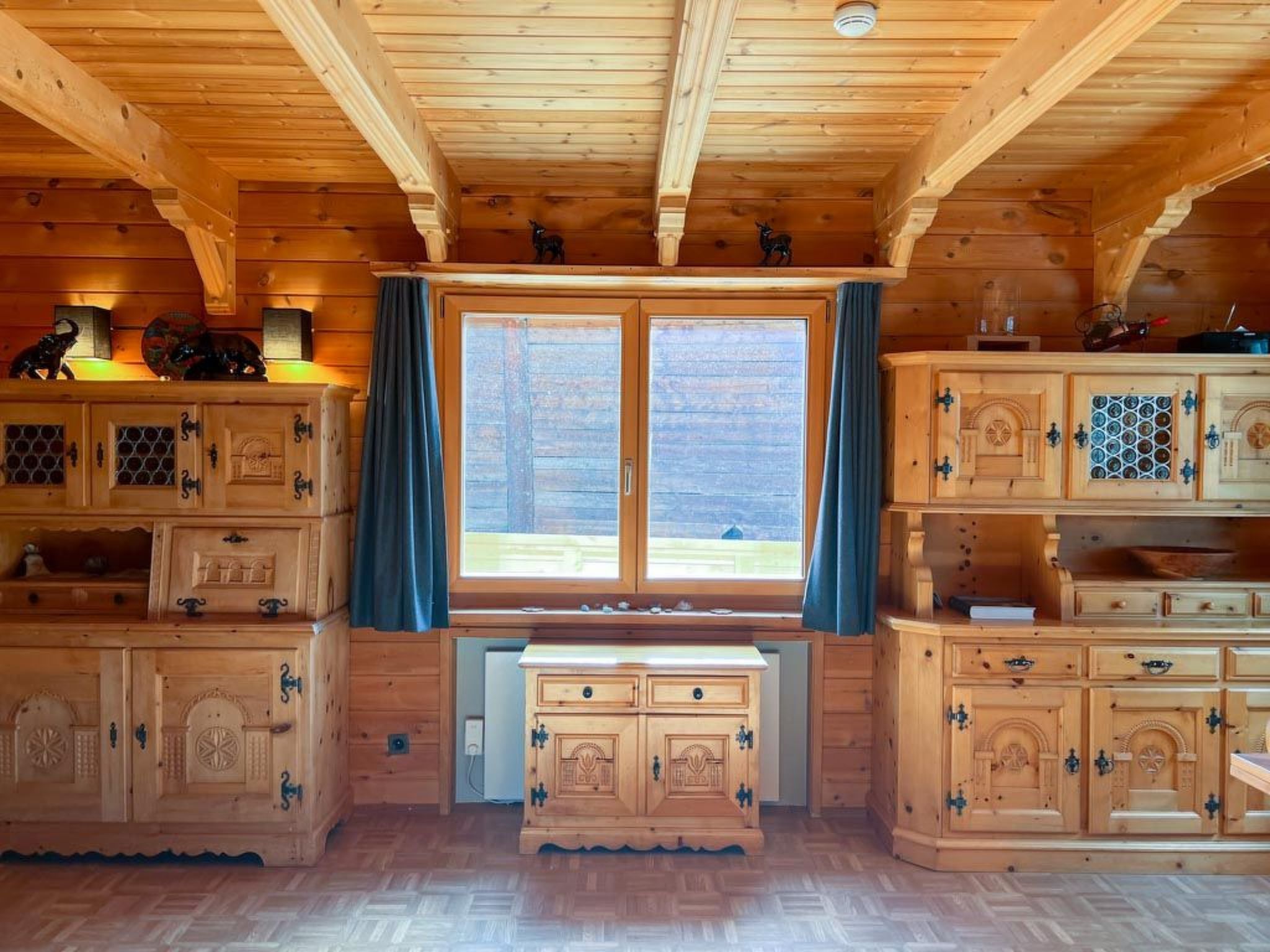 Interior d'una cabana de fusta amb un gran finestral, armaris de paret i un paviment amb motius de serra.