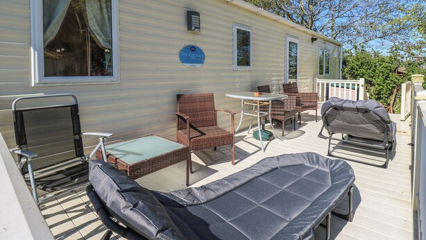 Een stacaravan met een terras, compleet met een tafel, stoelen, een ligstoel en een barbecue.