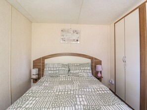 A bedroom with a bed, a nightstand, a bedside lamp, a wardrobe, and a wall decoration. - Valley Farm Number 448 (Clacton-on-Sea)