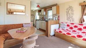 Een compact woongedeelte met een kitchenette, een eethoek en een slaapbank met een bloemenprint.