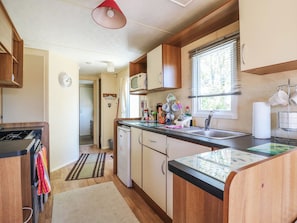 A compact kitchen with a microwave, sink, and wooden cabinets. - Valley Farm Number 448 (Clacton-on-Sea)