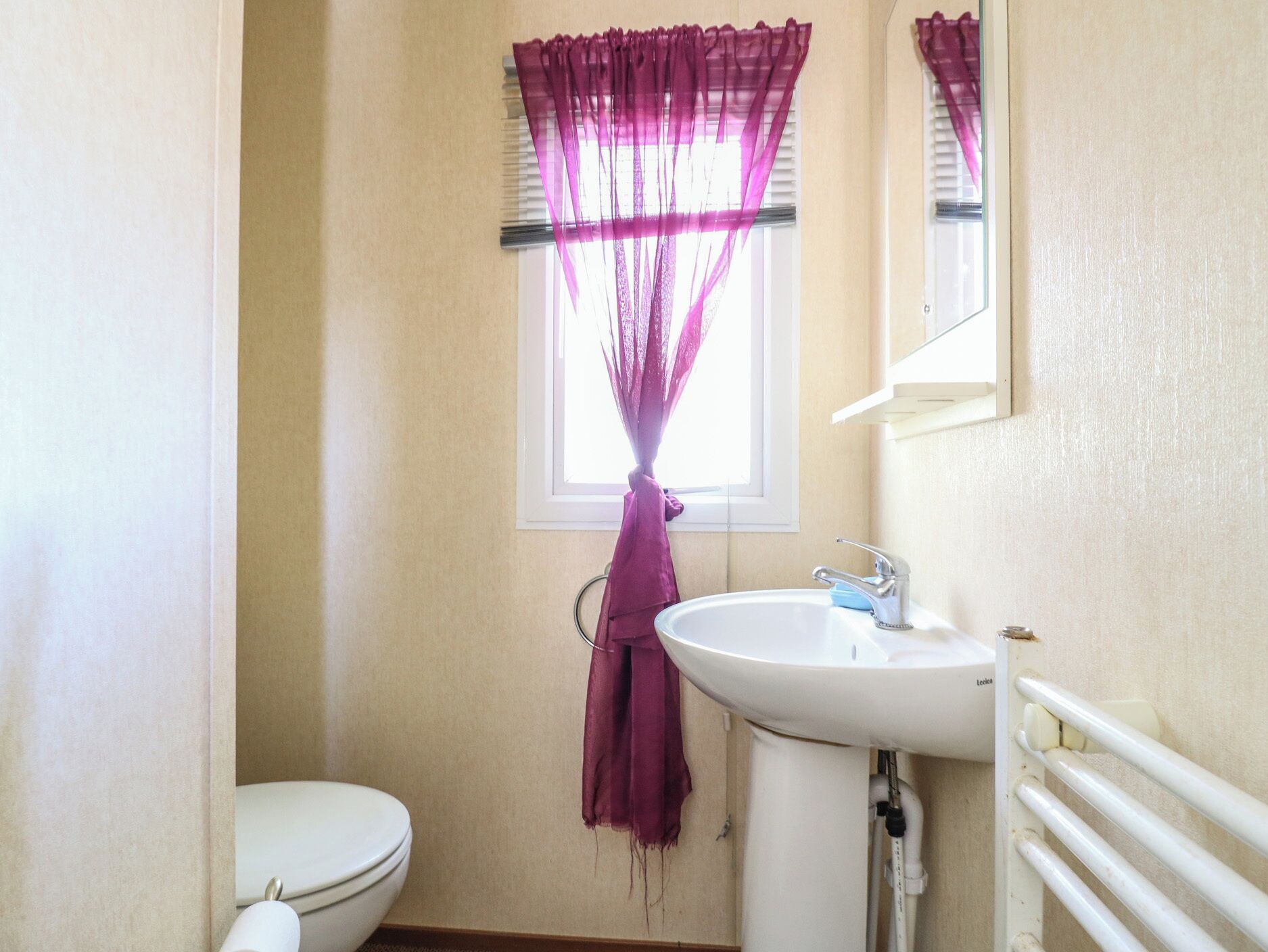 Une salle de bain avec des toilettes, un lavabo et une fenêtre ornée de rideaux violets.