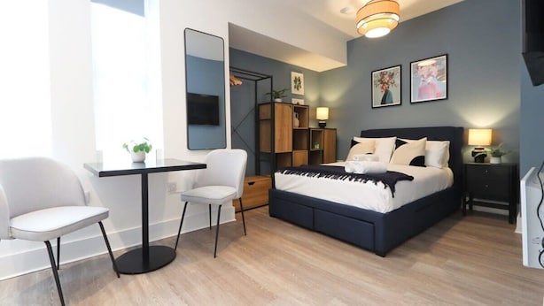 Ein modernes Schlafzimmer mit Bett, Nachttischen, Schreibtisch, Stühlen und einem großen Spiegel.
