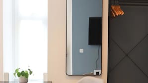 Ein modernes Zimmer mit einem großen Spiegel, einem Sessel, einem Tisch mit Topfpflanze, einem Kleiderständer und einem Fernseher.