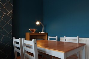 Ein Essbereich mit einem Holztisch und weißen Stühlen, einer Lampe und einer Schüssel auf dem Tisch.