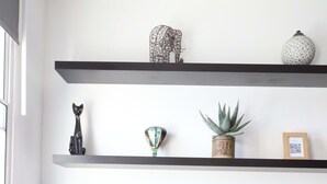 A living room with a TV on a wooden stand, two shelves with decorative items, and a potted plant. - Stylish 2 Bed in Old Market (Bristol)