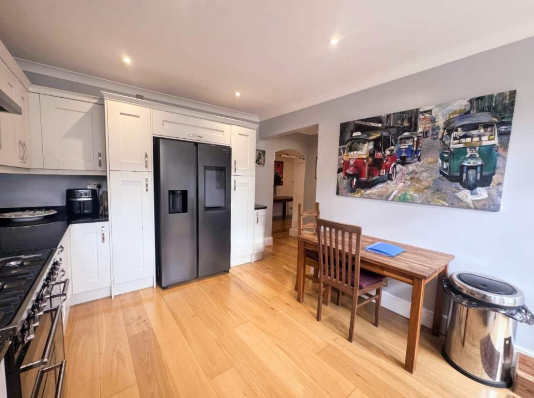 A compact kitchen with a dining area, a refrigerator, a stove, and a painting on the wall.