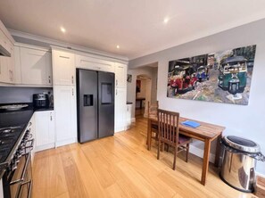 A compact kitchen with a dining area, a refrigerator, a stove, and a painting on the wall. - On Bedroom Redland retreat Parking (Bristol)