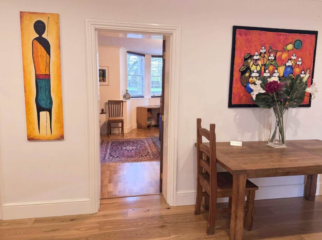 A dining area with a wooden table and chairs, a vase with flowers, and two paintings on the walls.