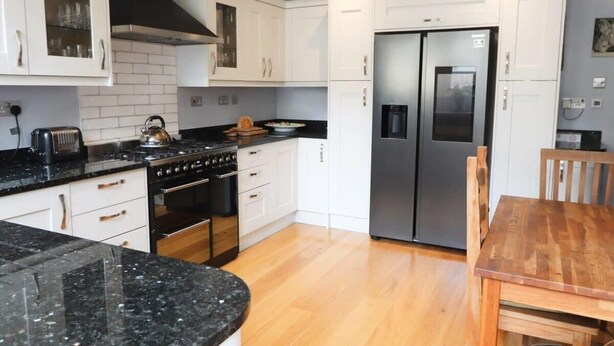 Een moderne keuken met witte kasten, een roestvrijstalen koelkast, een houten eettafel en een zwart aanrecht.