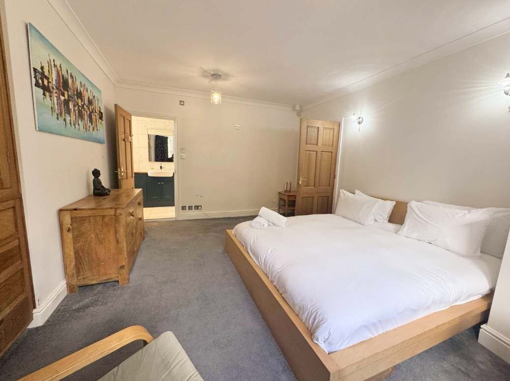 A bedroom with a large bed, wooden dresser, and a painting on the wall.