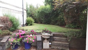 Een tuin met een houten terras, plantenpotten en een stenen vogelbad.