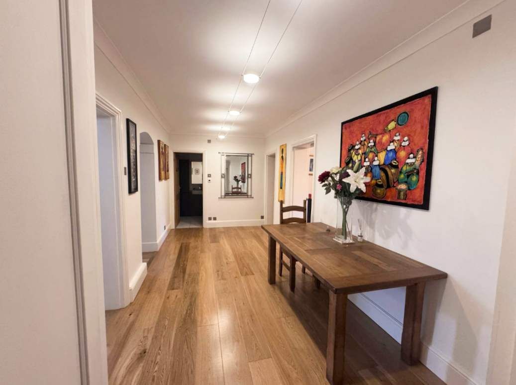 Een gang met een houten vloer, een eettafel, stoelen en een schilderij aan de muur.