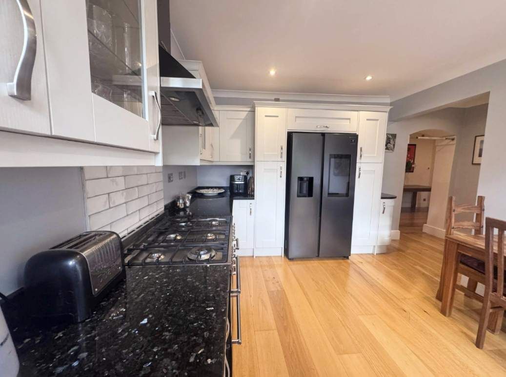 Een moderne keuken met witte kasten, een zwart aanrecht, een roestvrijstalen koelkast en een houten eettafel.