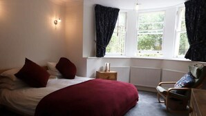 Een slaapkamer met een bed, nachtkastje, stoel en een raam met gordijnen.